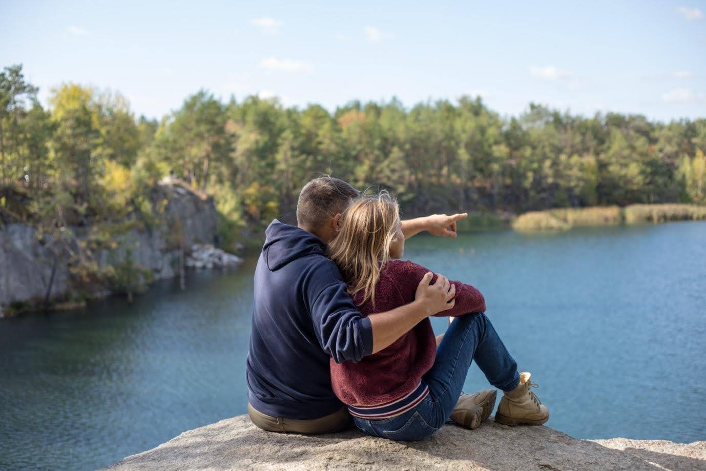 codependency meaning in relationships, a couple sitting on a rock overlooking a lake.